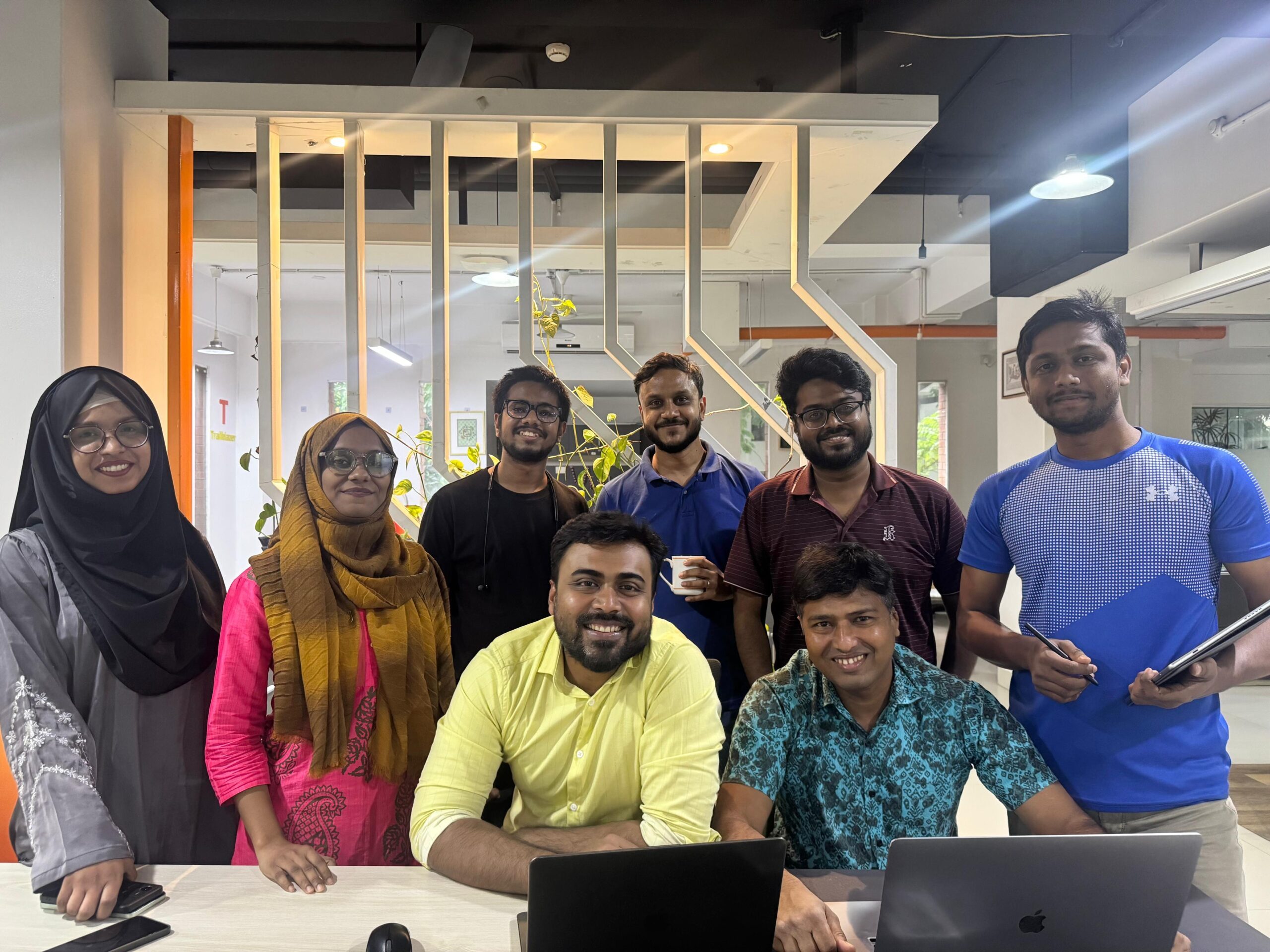 Group of Bangladeshi students and faculty gather around a laptop.